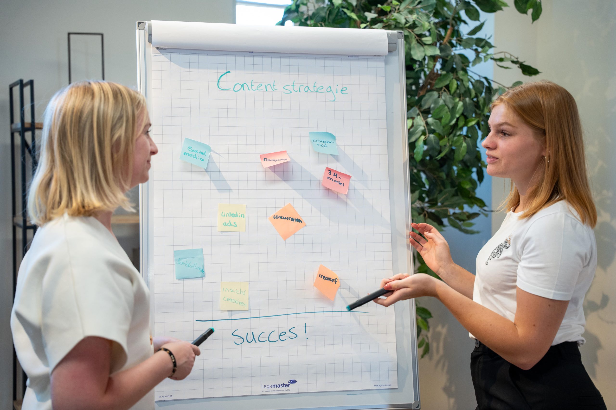 2 vrouwen bij flip-over bord met een contentstrategie en post-its erop
