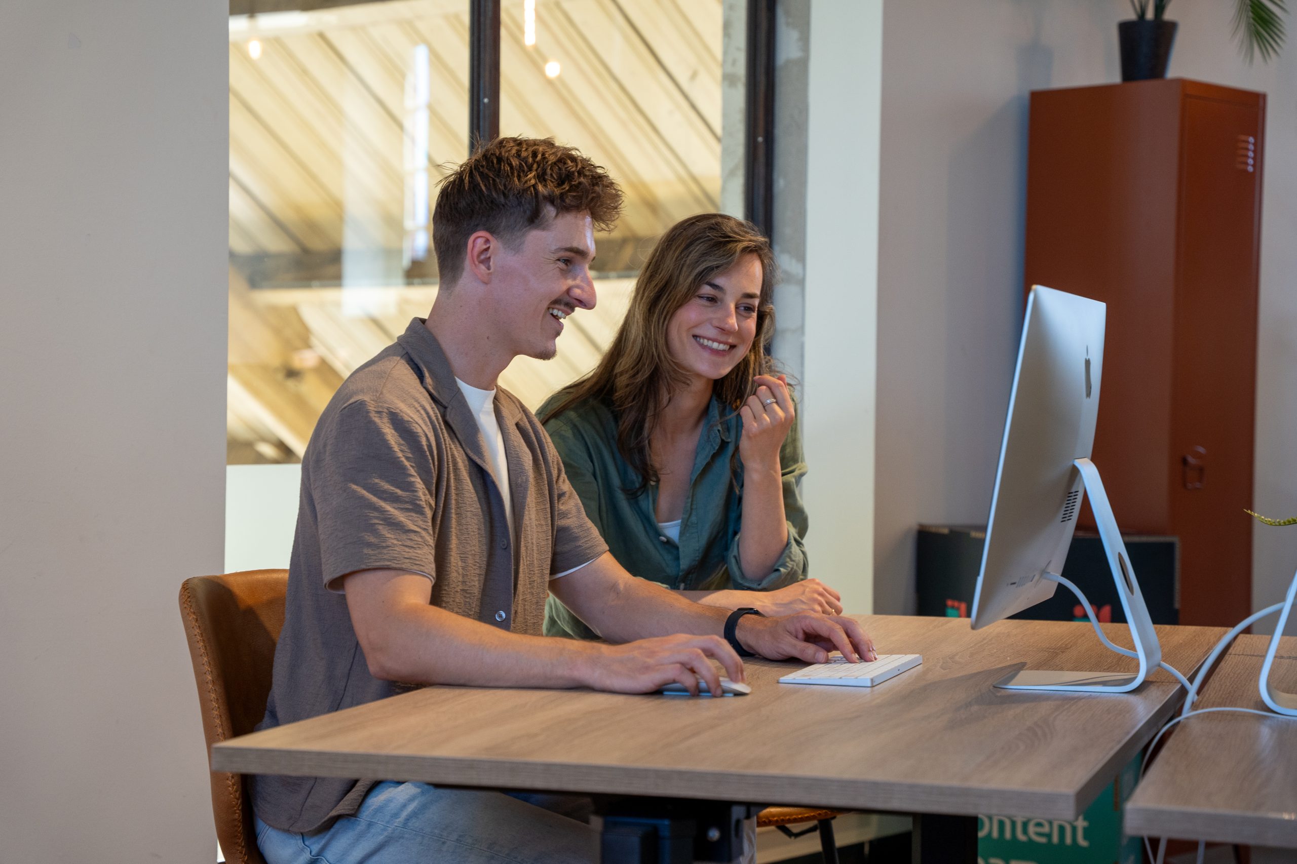 Jordi en Iris zitten samen lachend achter een computer aan een bureau.