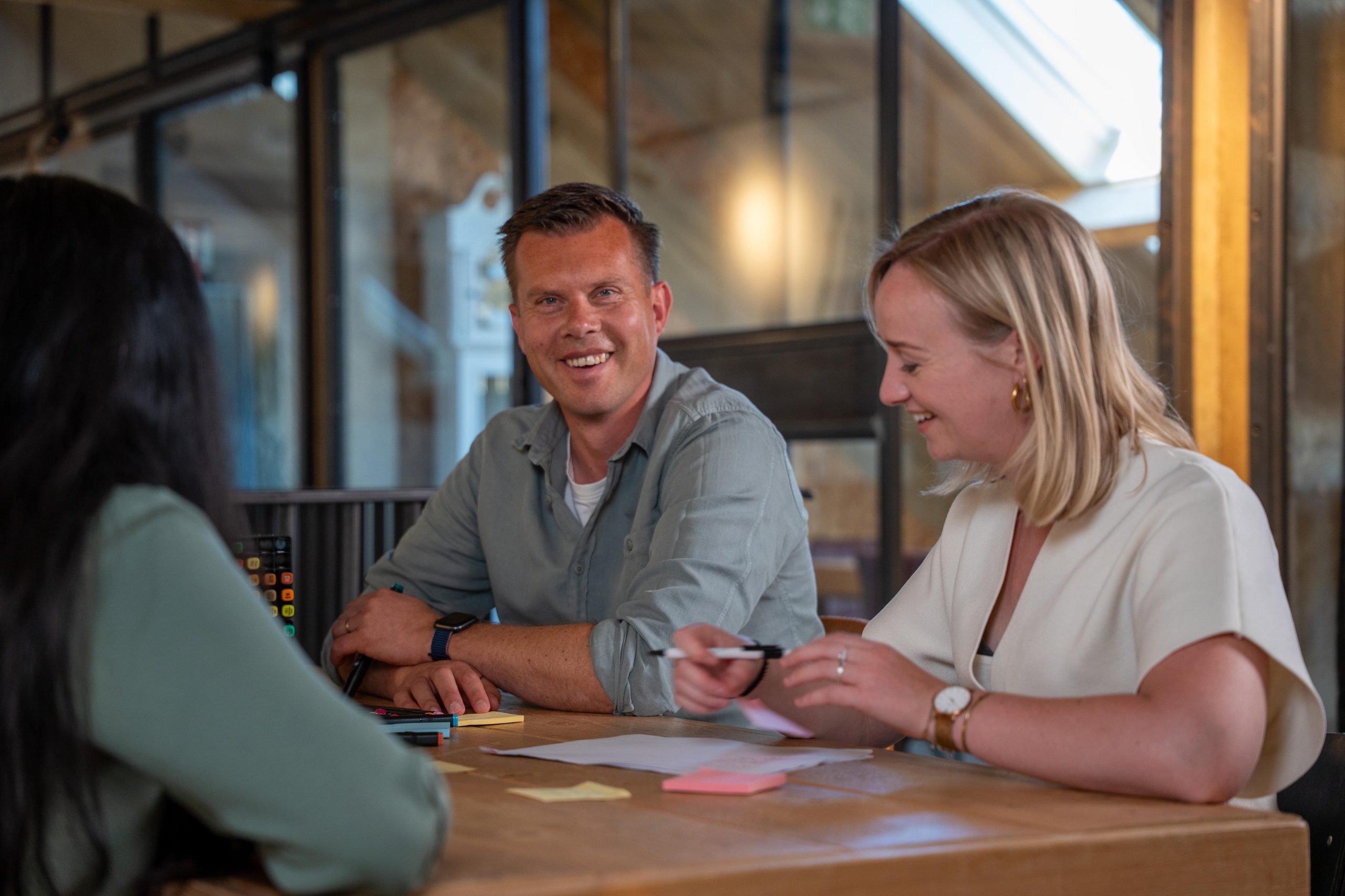 Lachende collega’s overleggen met stiften en post-its aan tafel.